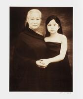 A sepia-toned photograph of an older woman and a young girl wearing dark clothes against a dark background.  They hold hands and look directly at the viewer.