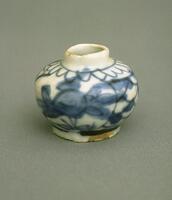 A small jar with a slightly tapered base and a shoulder that tapers to a narrow tall neck with a direct rim.  It is painted with underglaze cobalt blue floral designs, and covered in a clear glaze. 