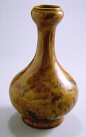 A stoneware jar with brown mottled glaze. It is on a thick footing and has a bulging bottom with a long neck and a smaller bulging rim.