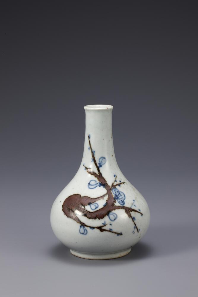 Many white porcelain bottles of this type were produced at Bunwon-ri in the 19th century. One side of its body is decorated with a spray of plum blossom, with the stem and flowers rendered in underglaze iron brown and cobalt blue, respectively. The relatively vivid colors of iron and cobalt colors made the decorations highly effective. The entire foot was glazed, while the foot rim retains traces of fine sand spurs. The precipitation of ash deposits on one side has produced pale green spots. However, this is a high-grade object with transparent and well-fused glaze.<br />
[Korean Collection, University of Michigan Museum of Art (2014) p.180]