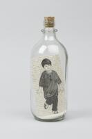 Glass bottle containing sand and a drawing a small boy sealed with a cork.