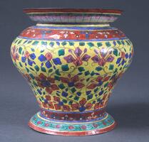 Cloisonne (metalwork with enamel decor) jar.  This jar uses brightly colored red, blue, green, yellow, and pinkish-purple enamelsto decorate its registers with intricate floral and vegetal patterns.  Mounted on a sturdy circular base, the body of the vase flares outward to its widest point, then curves inward more steeply toward the neck, from which a bowl-like mouth curves upwards.