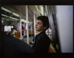 Portrait of a young man sitting on a subway train with his head leaning against the wall as he gazes pensively into the distance.