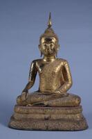 Gilt bronze Buddha with glass inlay in bhumisparsa mudra (the gesture of touching the earth with his right hand, palm inward), signaling his victory over Mara.  He has elongated earlobes, wears a crown and tight-fitting intricate robes, and is seated on a pedesal.