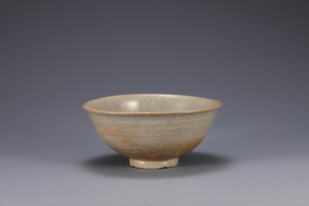 This is a whitel porcelain bowl with a flaring rim. The high iron content of clay and glaze used in white porcelain in the 17th century following the Japanese Invasion of Korea in 1592 (Imjim Warran) resulted in dark color of body, as it appears in this bowl. The foot features traces of coarse sand supports, while there are four sand spur marks on the inner bottom, suggesting that the bowl was stacked among other bowls during firing. Glaze running had formed on the outer surface in some parts and oxidized glaze tinged the overall surface with light yellow.<br />
[Korean Collection, University of Michigan Museum of Art (2014) p.162]
