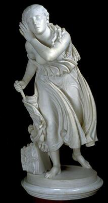 A white marble statue of a young female figure, leaning forward holding a staff with eyes closed, her left hand held up to her right ear. A flowing, wind-swept garment drapes the figure. On the base to the left of the figure is a broken capital of a Corinthian column lying on its side.