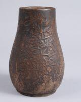 This brown vase has a raised design on the surface.  The vessel has a fairly wide mouth and gently swelling shape.