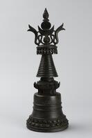 A miniature stupa, cast of bronze in several parts, consisting of a bell-shaped base; an inverted cone-shaped tower, capped by an "umbrella" with pendant, fringe-like decoration, inlaid with semi-percious stone, surmounted by a lotus bud. Atop the whole structure is a half-moon and sun disk motif, supported by intertwined ribbons and culminating in another lotus bud.