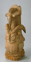 Wooden composite sculpture with the lower portion representing a ram's head and the upper half representing a bird, with its beak facing downwards. 