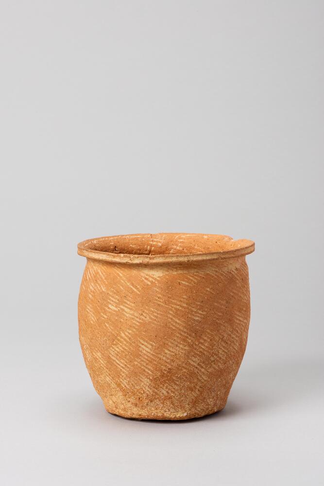 It has a outward-turned rim. The side of the body is almost straight. The bottem is flat. There is a comb pattern on the body surface.<br />
<br />
This is a reddish yellow, deep-bowl-shaped, low-fired earthenware vessel. Such vessels were generally used for boiling but this example contains no trace of use and is therefore likely to have come from a tomb. The vessel does not have a neck, the mouth is everted, and the flat edge of the rim features a groove. The vessel body is widest towards the upper-middle section, and the flat base is rounded where it joins the vessel body. The inner and outer surfaces of the vessel body show clear traces of paddling, but it is unclear whether these are cord-paddled markings. The base retains traces of the potter&rsquo;s wheel.<br />
[Korean Collection, University of Michigan Museum of Art (2017) p.45]<br />
&nbsp;