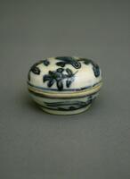 This small porcelain box has a base and the lid similar in size and shape, being round and shallow with curved sides. The box rests on a foot ring and is painted with underglaze cobalt blue to depict a duck and plants, covered in a clear glaze.