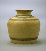 A small, flat-bottomed stoneware jar, with nearly straight sides flaring out to shoulders only slightly broader than the base, and narrowing to a short neck with an everted rim. The decoration consists of broad horizontal bands of cobalt blue pigment at the base, on the shoulder, and at the neck. The overall glaze, normally a whitish color, is a light brown here, possibly because of less than ideal conditions in the kiln.