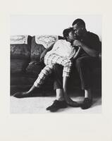 Black and white image of a man and woman sitting on a couch. The woman is leaning against the man and has one of her legs draped over one of his legs. He holds her hand. 