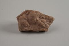 Terracotta fragment of two figures carved on one side of the peice in raised relief.  One figure has head and shoulders visible, the second figure has only the head visible.