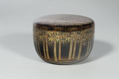 Cylindrical container with a detachable lid. The container and lid are painted black with black and gold bamboo designs on the exterior and gold splatters on the interior.&nbsp;