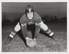 A black and white image of a man in a football uniform holding a football to the ground.