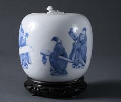 This white porcelain jar has the design of six Chinese sages and an attendant boy with blue underglaze in delicate brushwork. One sage is reading a book, while another is listening. The attendant boy is standing next to the sage with a book. Other four sages are looking at a long hand scroll. Some sages hold staffs on their hands. One sage has a string instrument. The jar has a broad shoulder and an inverted mouth, where the lid is placed. The knob of the lid is in a shape of a reclining boy (unpainted), surrounded by books, hanging scrolls, a cane, and a fan, which are painted with blue underglaze. It also has a shallow foot.
