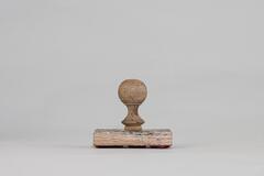 Carved rubber stamp with a rectangular wooden base and rounded handle. The handle is a faded blue color and there is ink residue on the stamp surface.