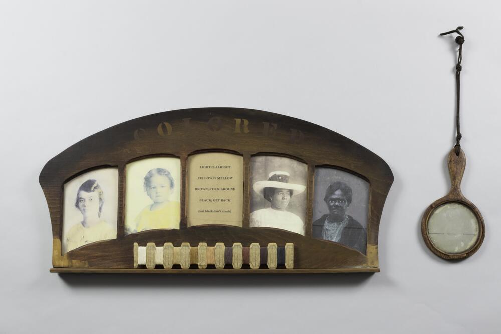 An assemblage of found objects: a salvaged wood frame with wood inlay letters spelling &quot;COLORED,&quot; four portrait photographs of African American females (two photogaphs on either side of a printed poem), nine thread samples under photographs, and one hand mirror hanging on a decorative brass hook to the viewer&#39;s right of the frame. The poem reads:&nbsp;<br />
&quot;Light is Alright<br />
Yellow is Mellow<br />
Brown, Stick Around<br />
Black, Get Back<br />
(but black don&#39;t crack)&quot;<br />
<br />
The wood has a strong smell, may have been treated with molasses.<br />
<br />
&nbsp;